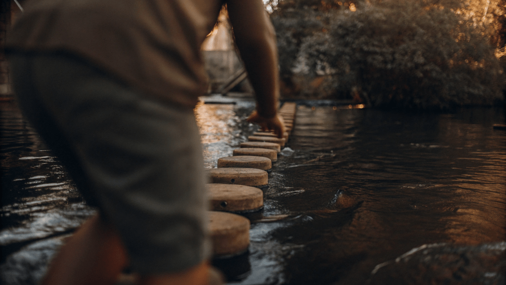 someone carefully crossing a river using stepping stones to show that step by step we make progress