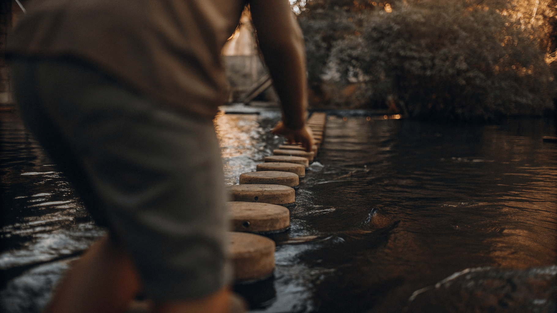 someone carefully crossing a river using stepping stones to show that step by step we make progress